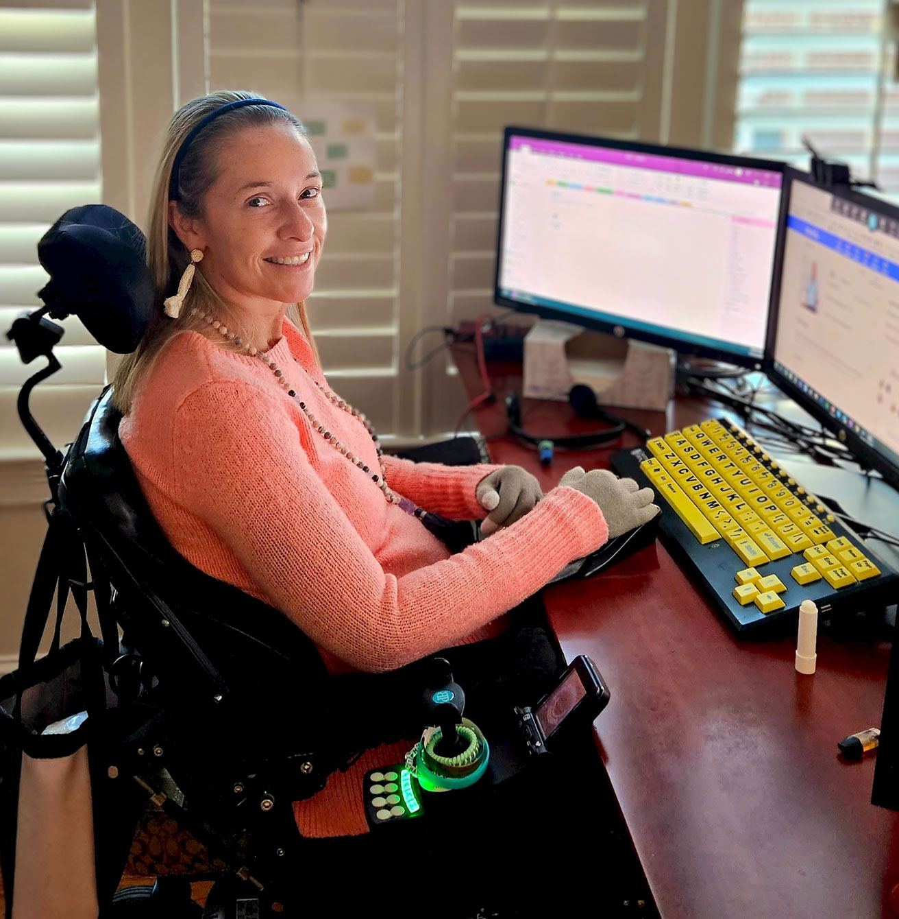Ali smiling seated in her wheelchair in front of her computer.