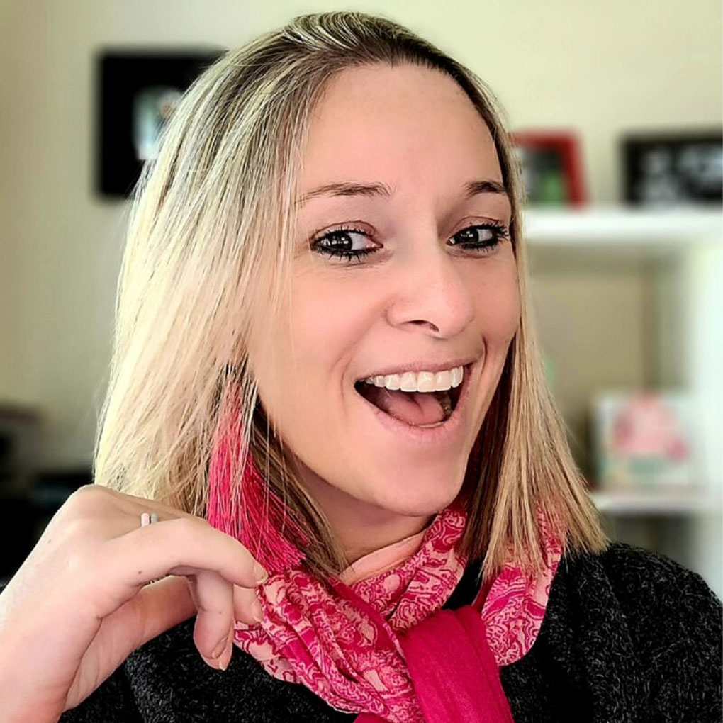 Ali smiling big wearing a pink scarf and blonde hair